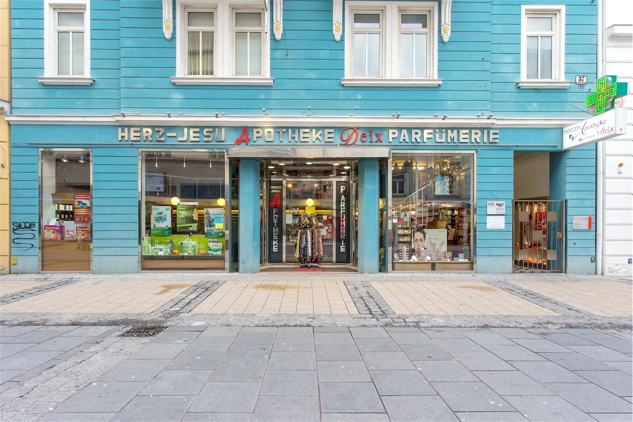 Türkisfarbene Fassade in der Kremser Gasse 37 mit dem Schriftzug „Herz-Jesu Apotheke Deix Parfümerie“ und grünem Apothekenkreuz